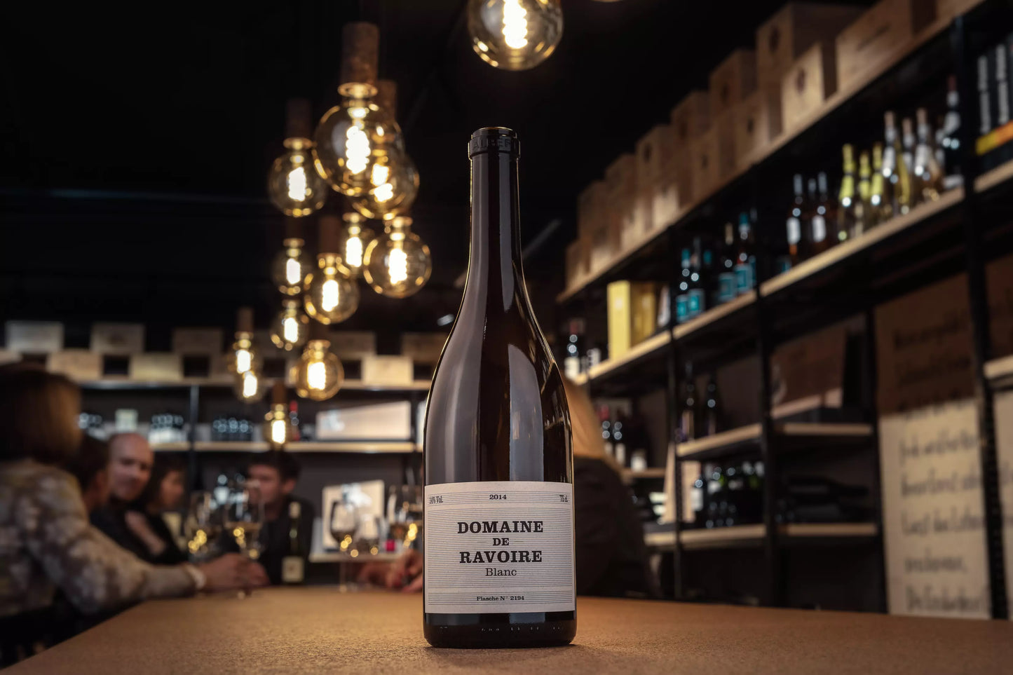 Domaine de Ravoire Blanc auf dem Tisch in der Vinothek Hauser mit Apéro-Gästen im Hintergrund.