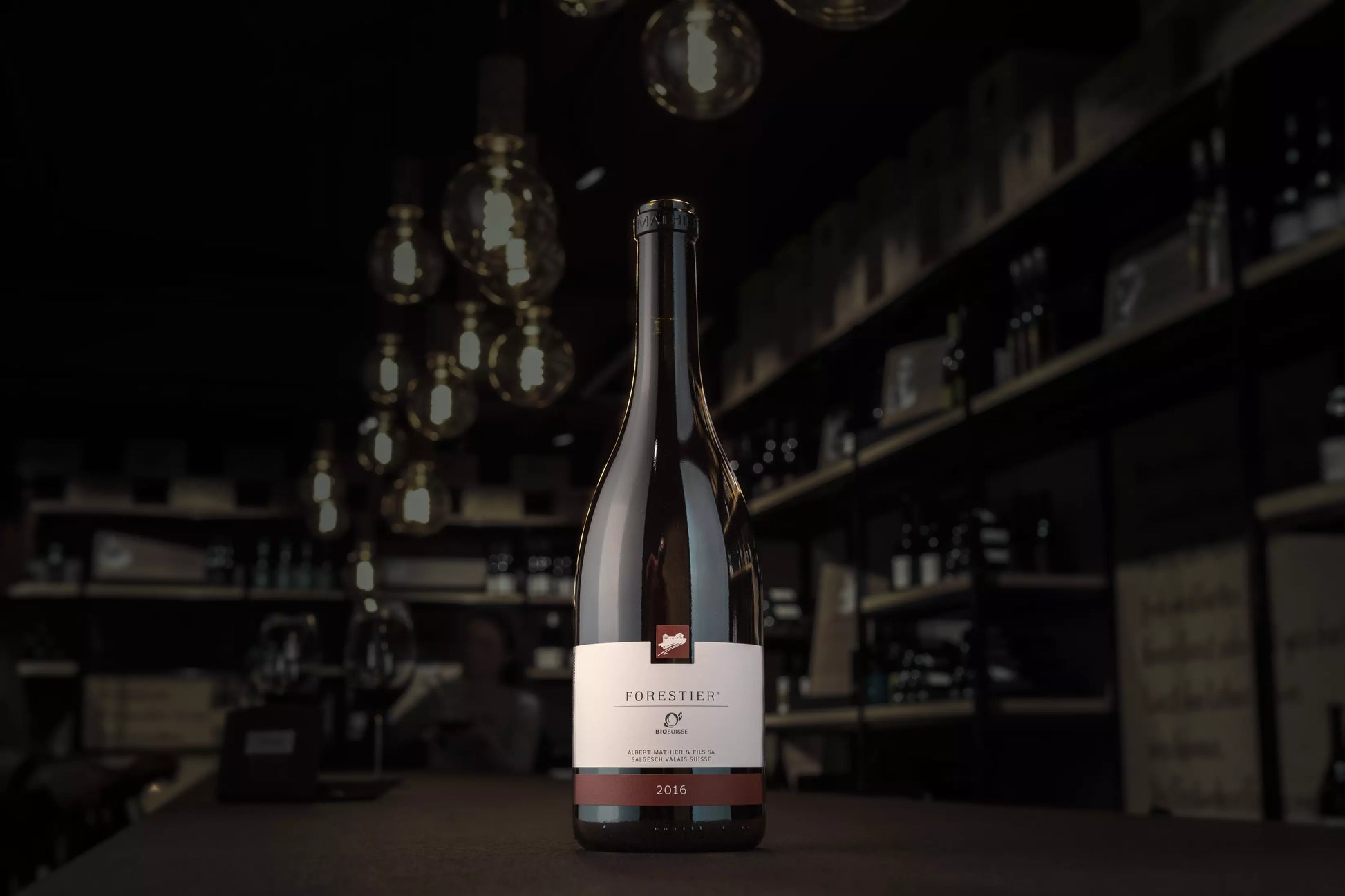Dunkle Vinothek Hauser, im Vordergrund auf dem Tisch eine Flasche Forestier Pinot Noir von Albert Mathier.