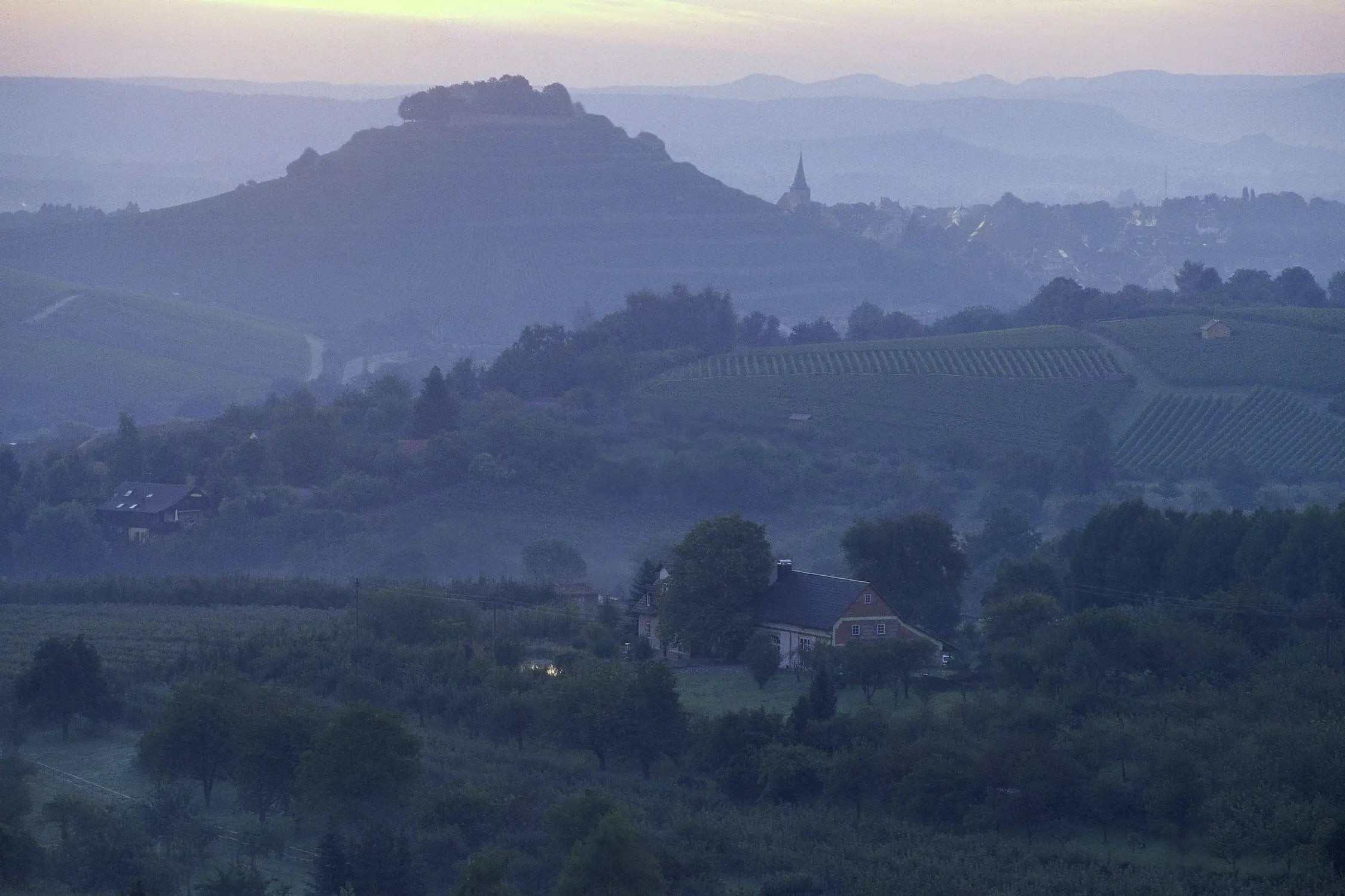 Blick über Weinberge mit Dorf und Bergen im Hintergrund im Sonnenuntergang im Anbaugebiet Württemberg.