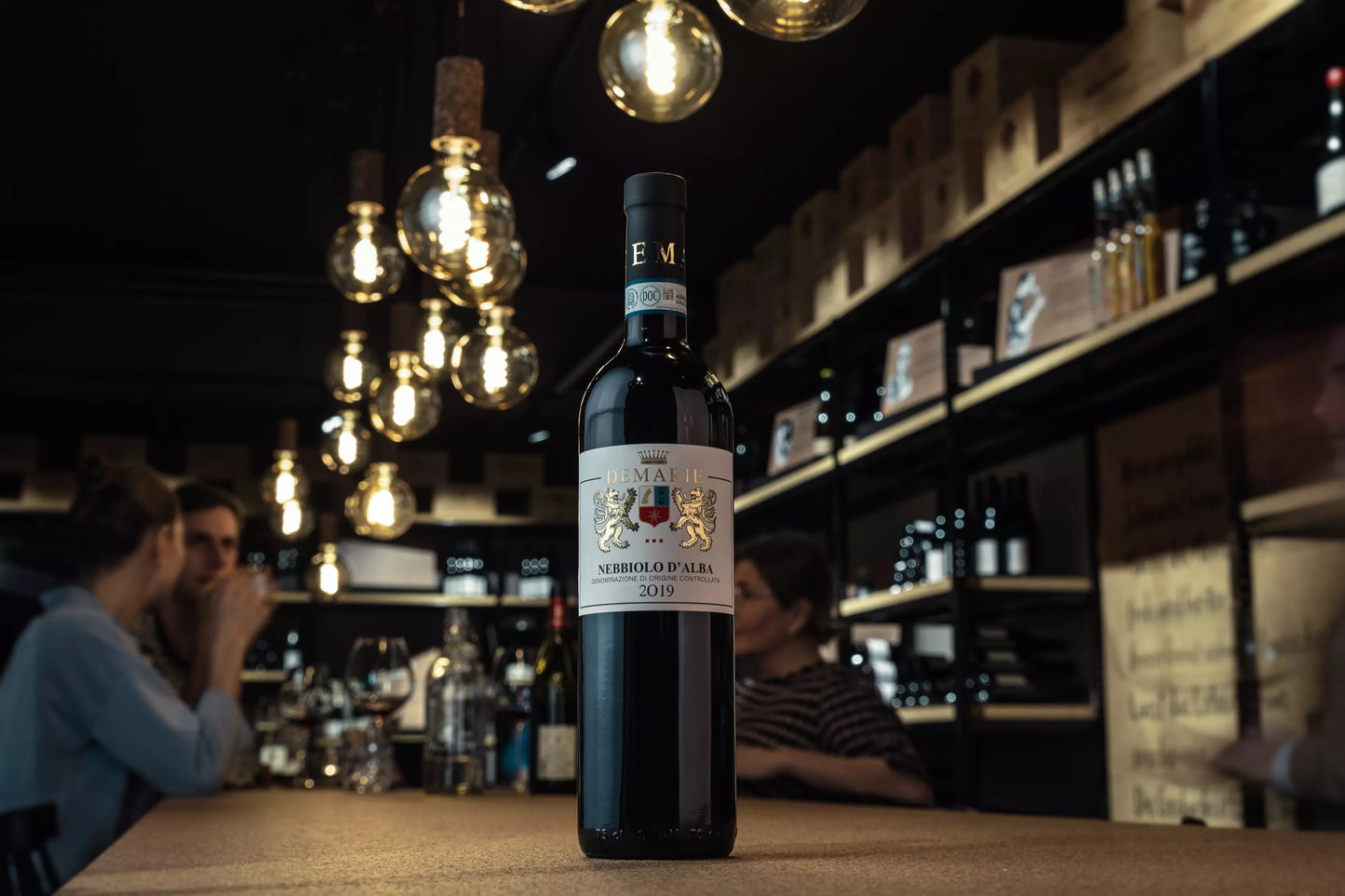 Nebbiolo d'Alba von Demarie auf dem Tisch in der Vinothek Hauser mit Gästen im Hintergrund.