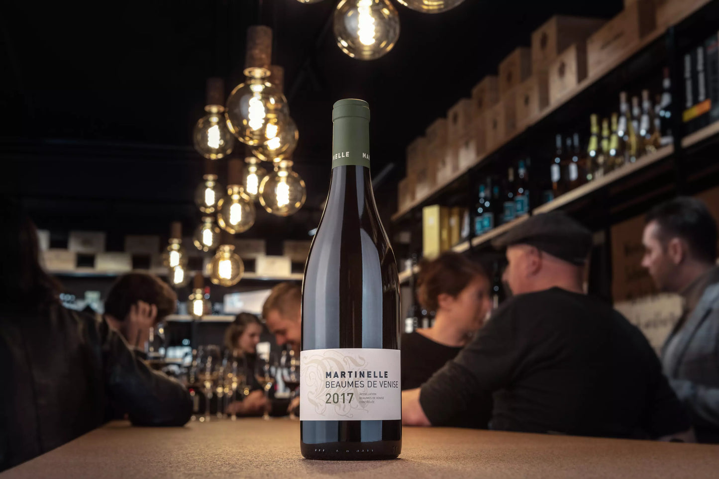 Beaumes de Venise von der Domaine Martinelle auf dem Tisch in der Vinothek Hauser mit Gästen beim Apéro im Hintergrund.