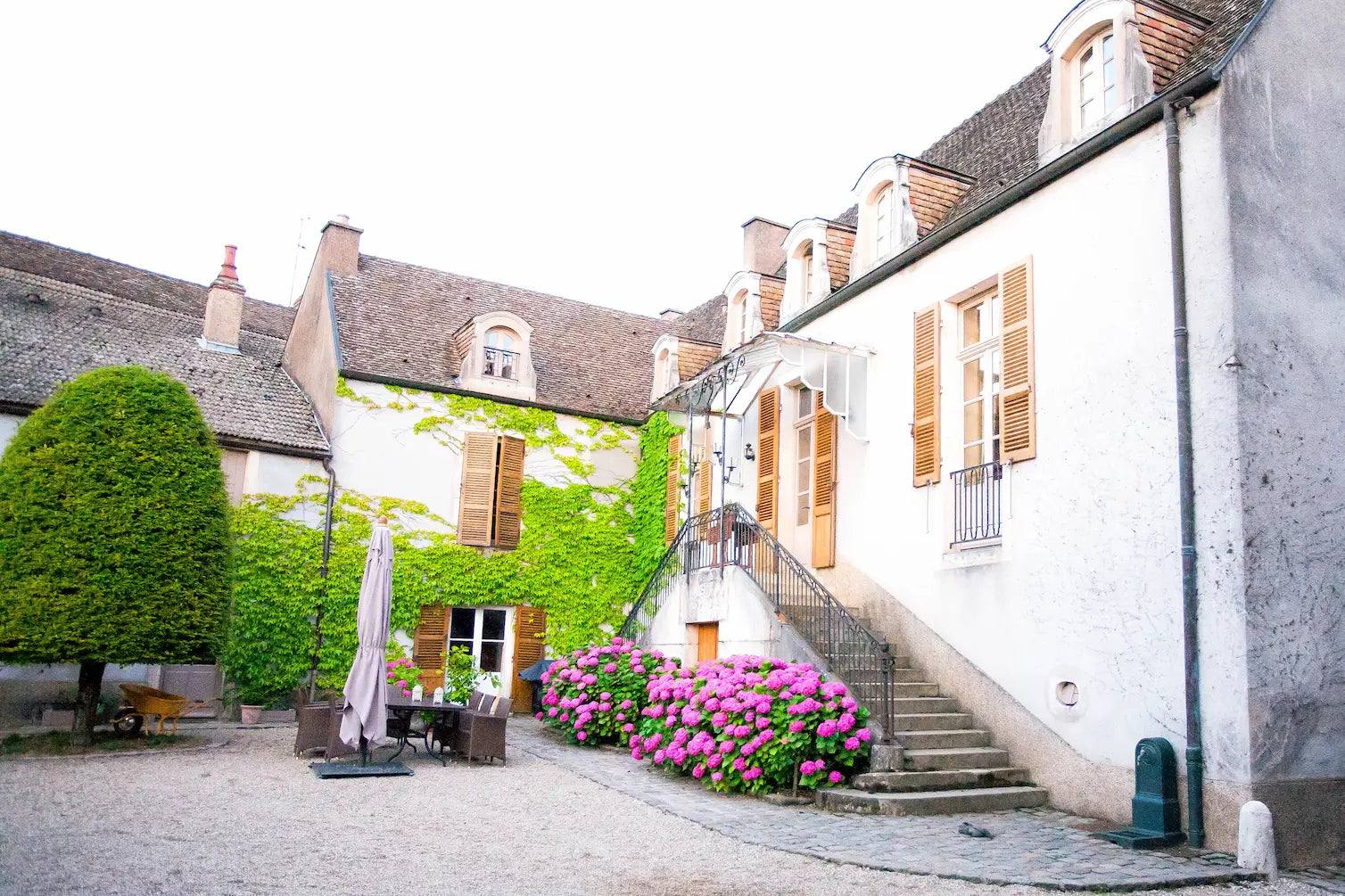Aussenaufnahme der Domaine Rougeot im Burgund im Sommer mit Blumen unterhalb der Einganstreppe und einer Sitzgruppe daneben.