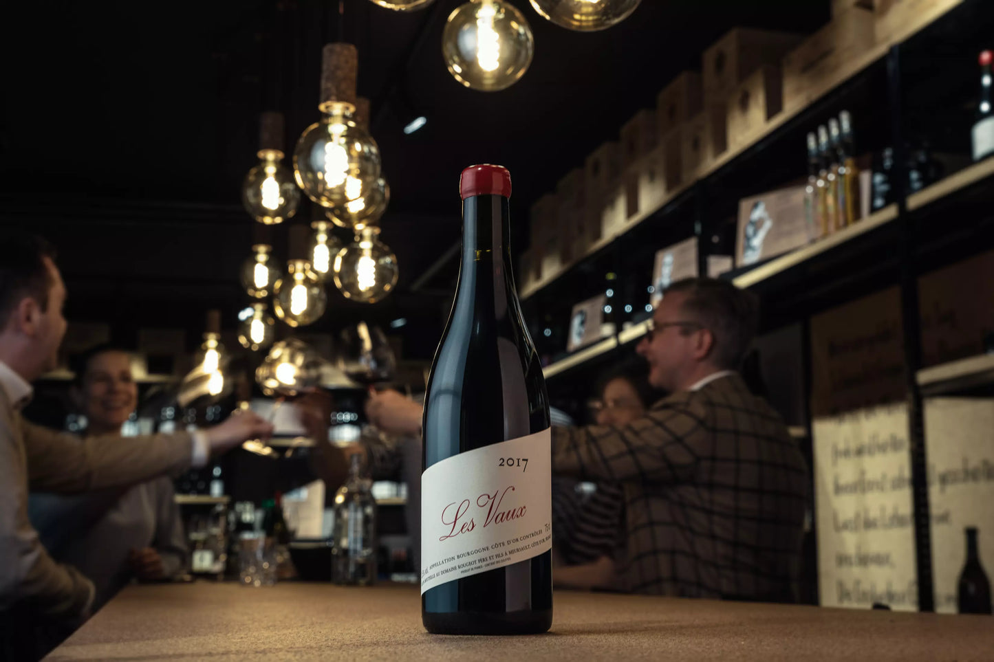 Bourgogne Pinot Noir Les Vaux von der Domaine Rougeot auf dem Tisch in der Vinothek Hauser mit Gästen im Hintergrund.