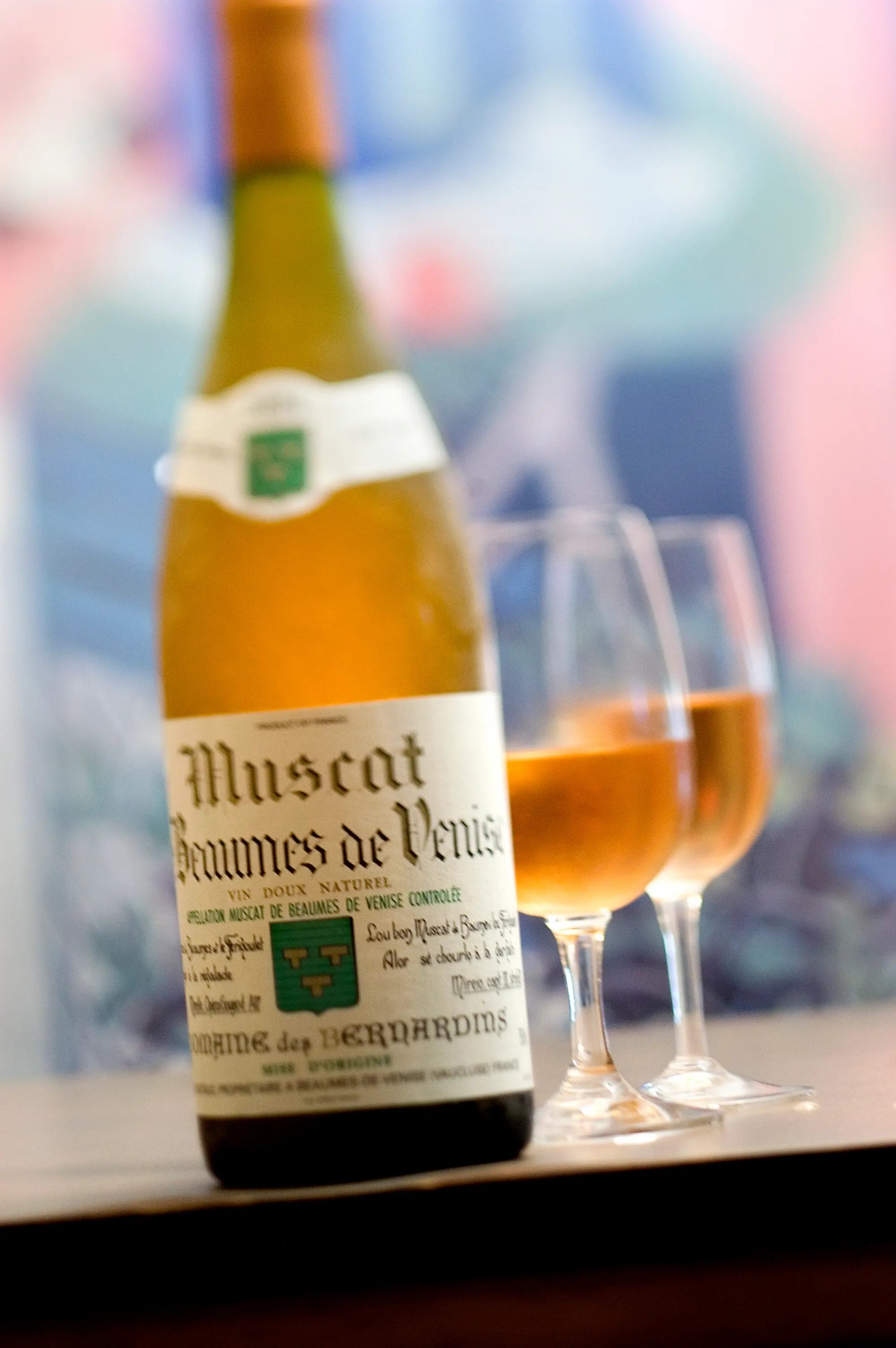 Flasche Beaumes de Venise von der Domaine des Bernardins mit zwei eingeschenkten Gläsern im Hintergrund.