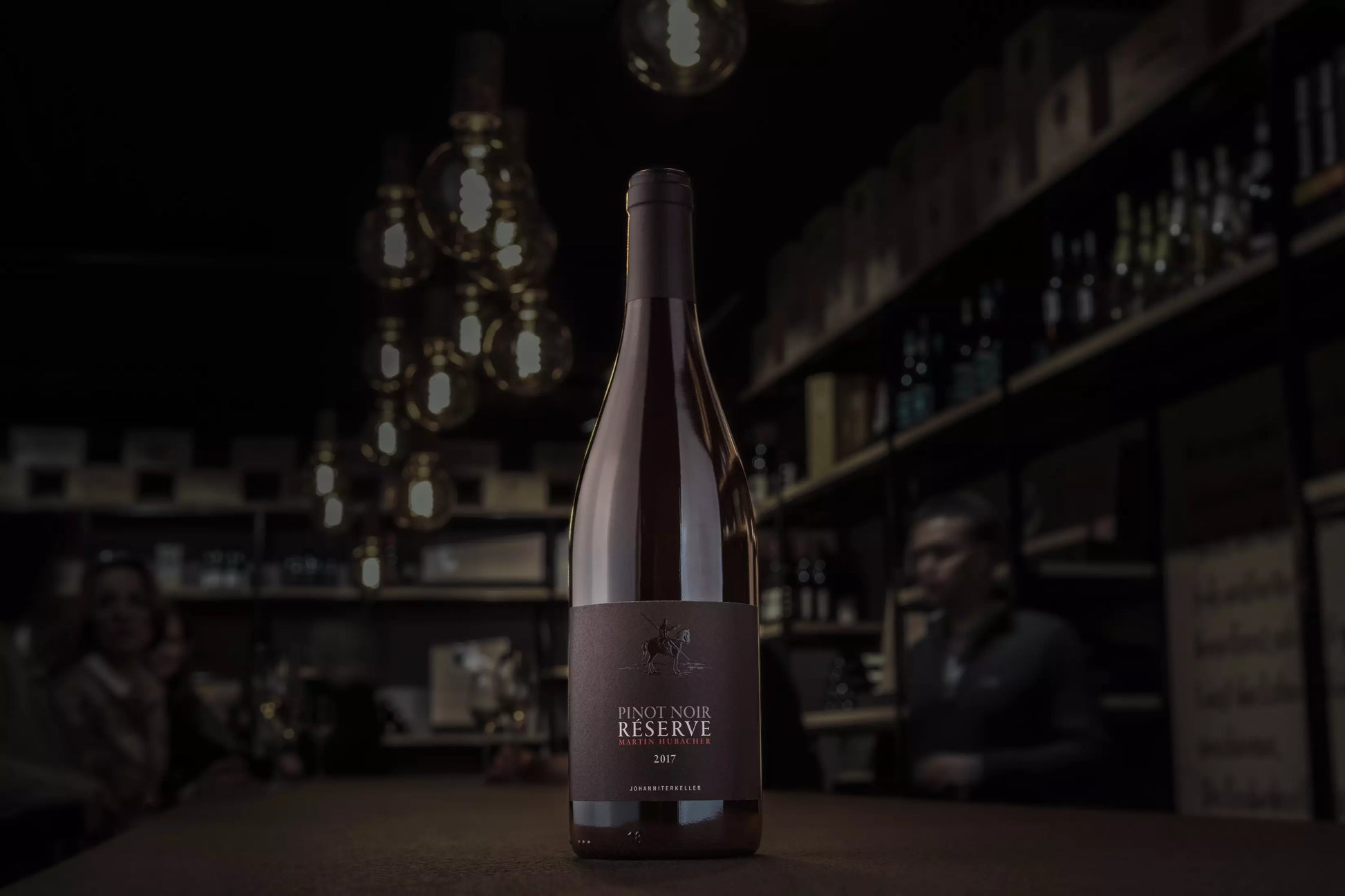 Pinot Noir Réserve vom Johanniterkeller Martin Hubacher auf dem Tisch in der Vinothek Hauser mit gedämmtem Licht.