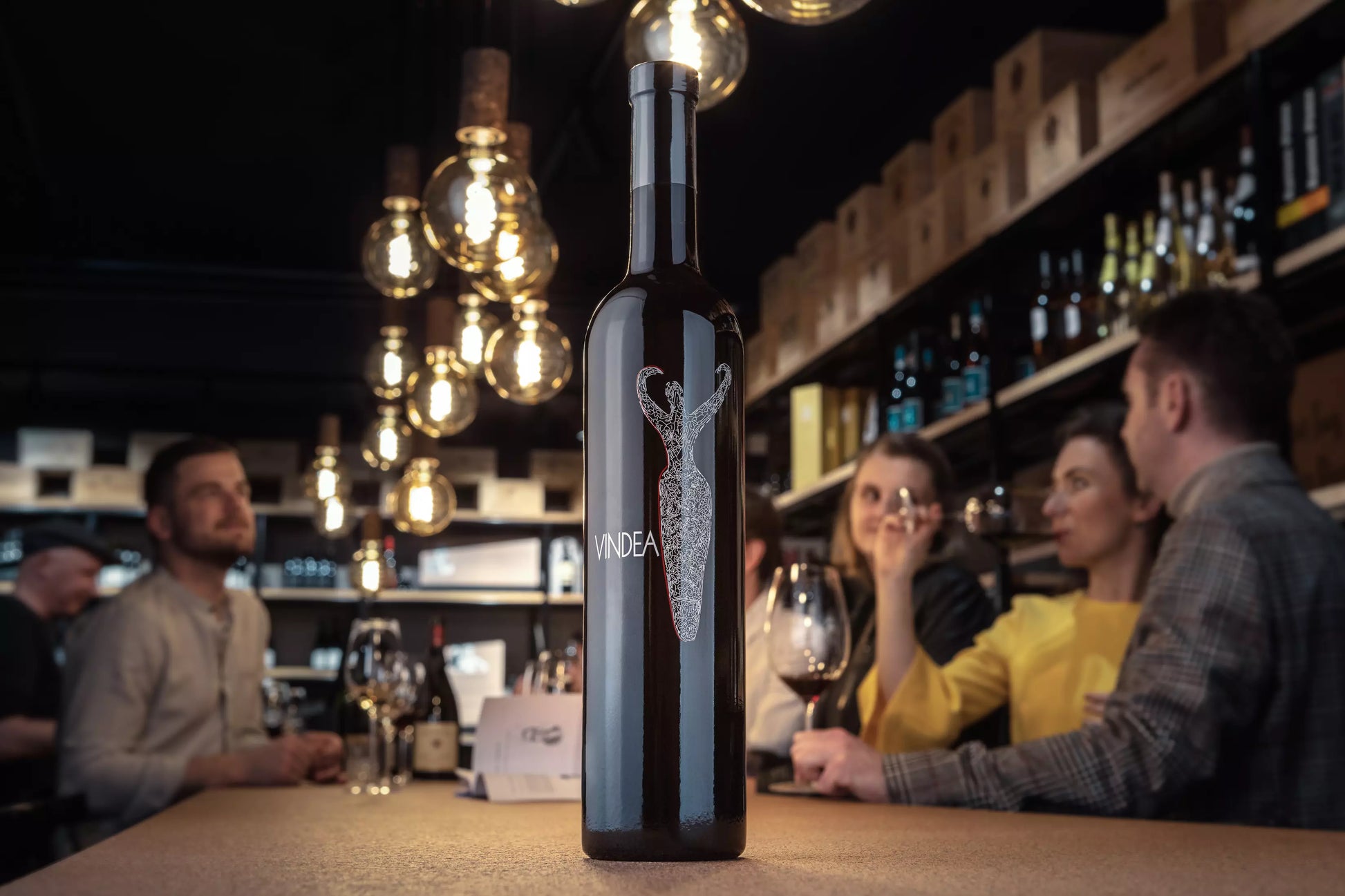 Vindea von Panzanello in der Toskana auf dem Tisch in der Vinothek Hauser mit Gästen beim Apéro im Hintergrund.