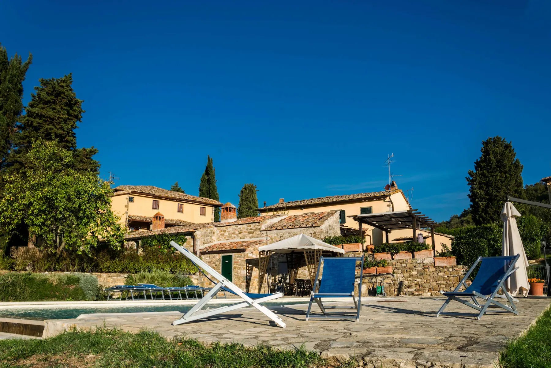 Aussenaufnahme vom Weingut Panzanello in Panzano in der Toskana mit Liegestühlen und Pool im Vordergrund.