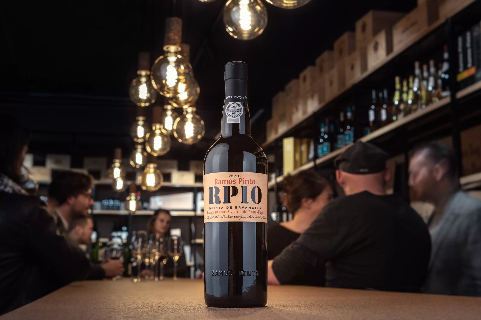 Flasche Porto 10 years von Ramos Pinto auf dem Tisch in der Vinothek Hauser mit einem Apéro, der im Hintergrund stattfindet.