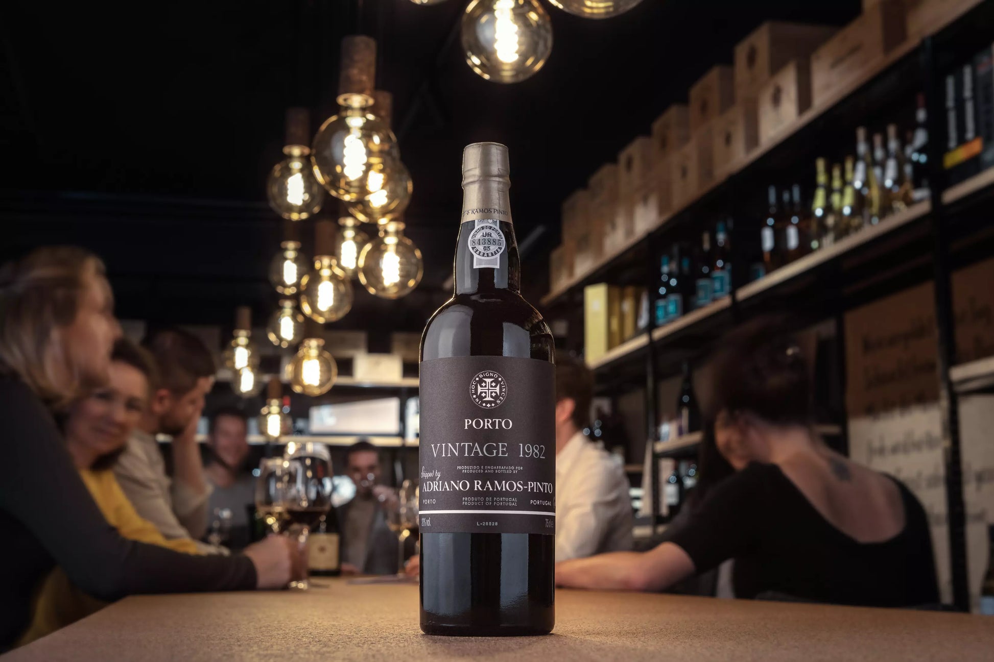 Flasche Vintage Port von Ramos Pinto auf dem Tisch in der Vinothek Hauser mit Gästen im Hintergrund.