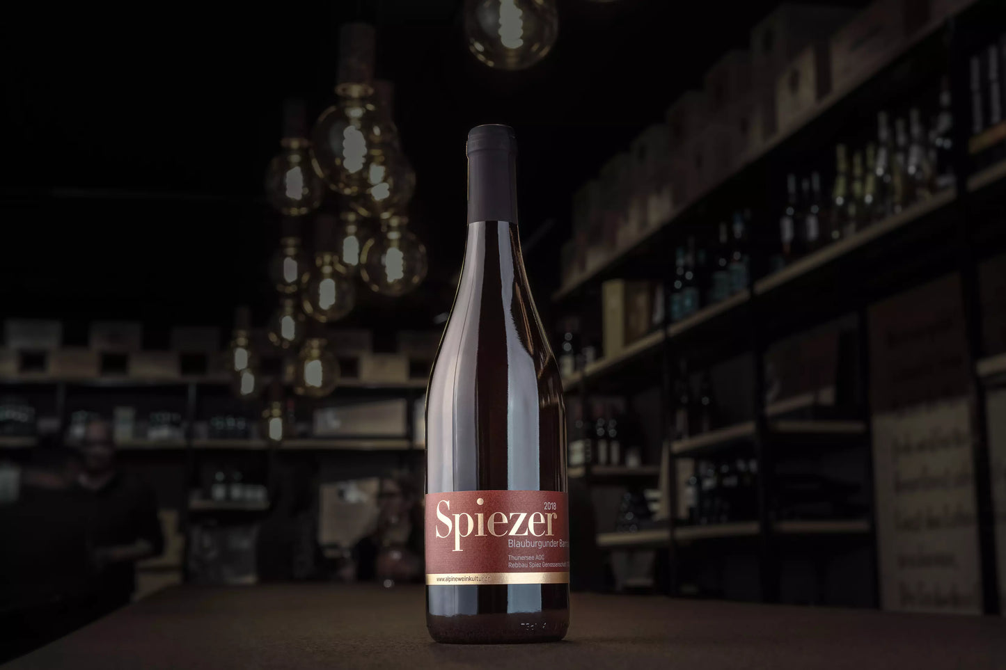 Spiezer Blauburgunder Barrique von Alpine Weinkultur Spiez auf dem Tisch in der dunklen Vinothek Hauser.