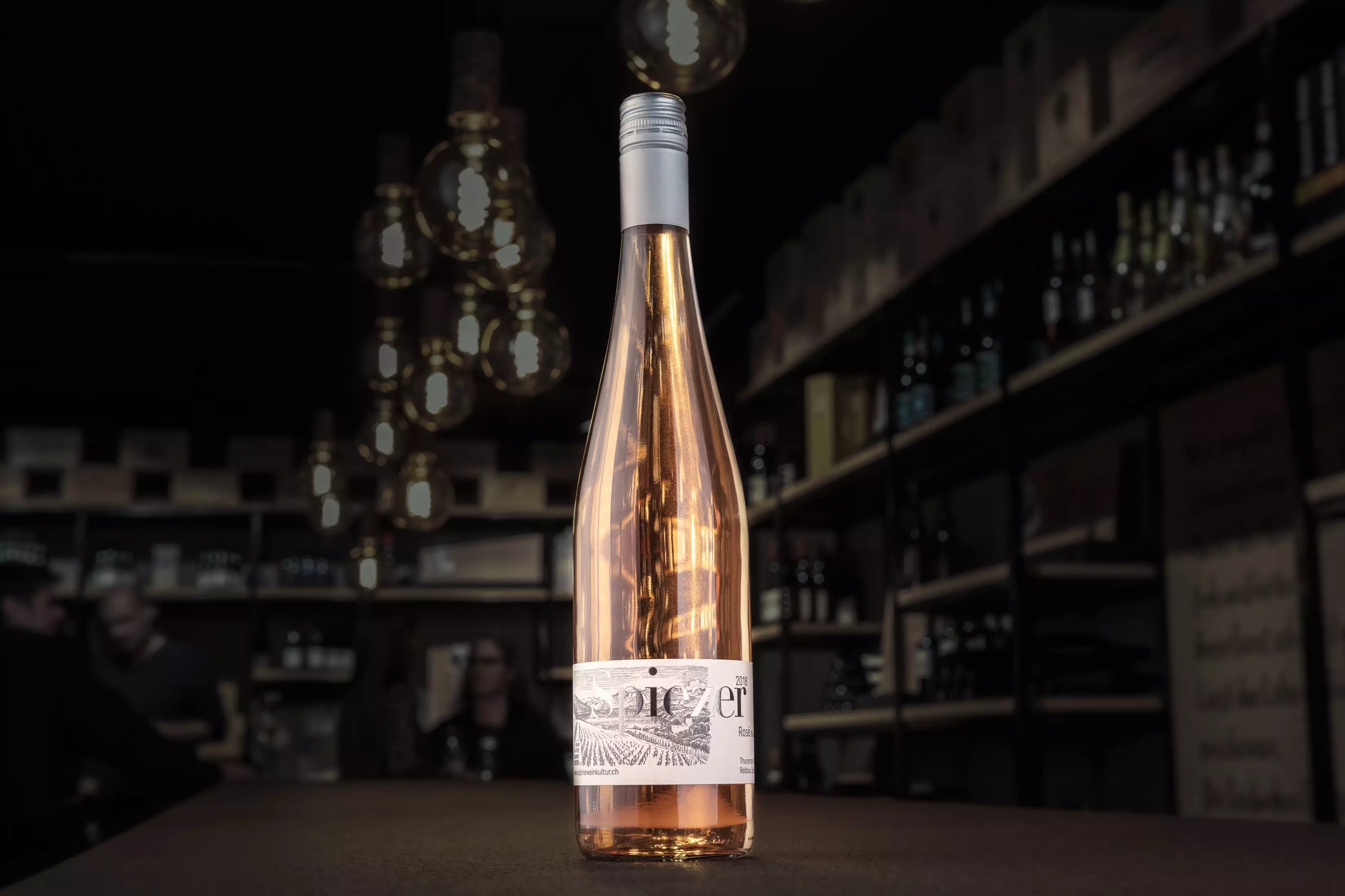 Spiezer Rosé von Alpine Weinkultur Spiez auf dem Tisch in der dunklen Vinothek Hauser.
