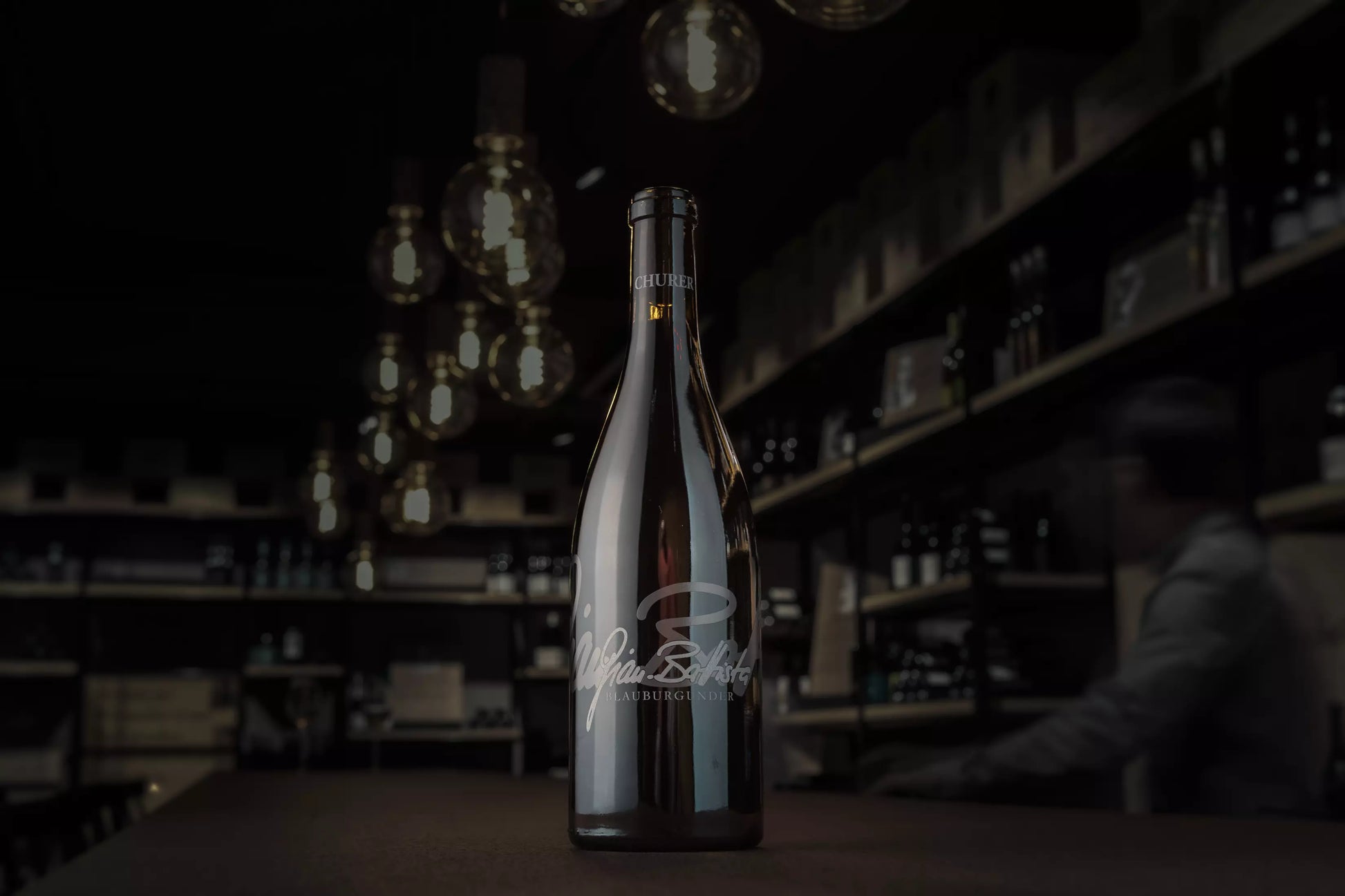 Churer Blauburgunder Gian-Battista von Weinbau von Tscharner in der dunklen Vinothek Hauser auf dem Tisch im Mittelpunkt präsentiert.