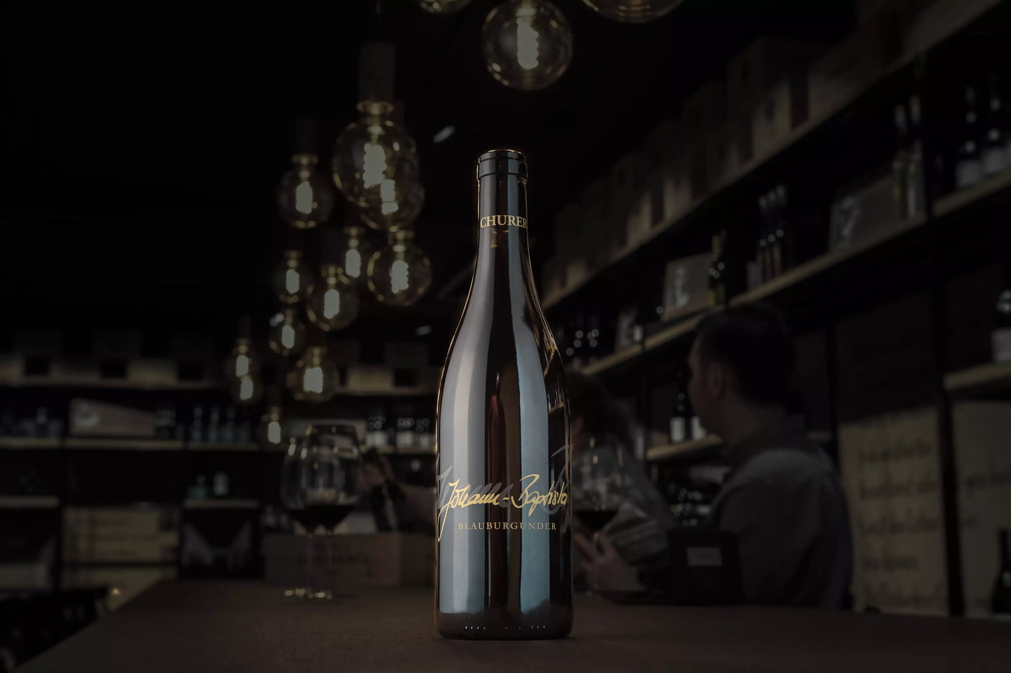 Churer Blauburgunder Johann Baptista von Weinbau von Tscharner auf dem Tisch in der dunklen Vinothek im Mittelpunkt.