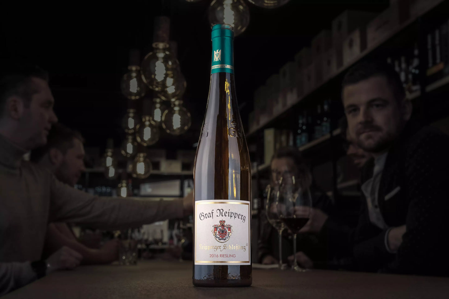Neipperger Schlossberg Riesling VDP.Grosses Gewächs vom Weingut Graf Neipperg in der Vinothek Hauser auf dem Tisch mit Gästen beim Apéro im Hintergrund.