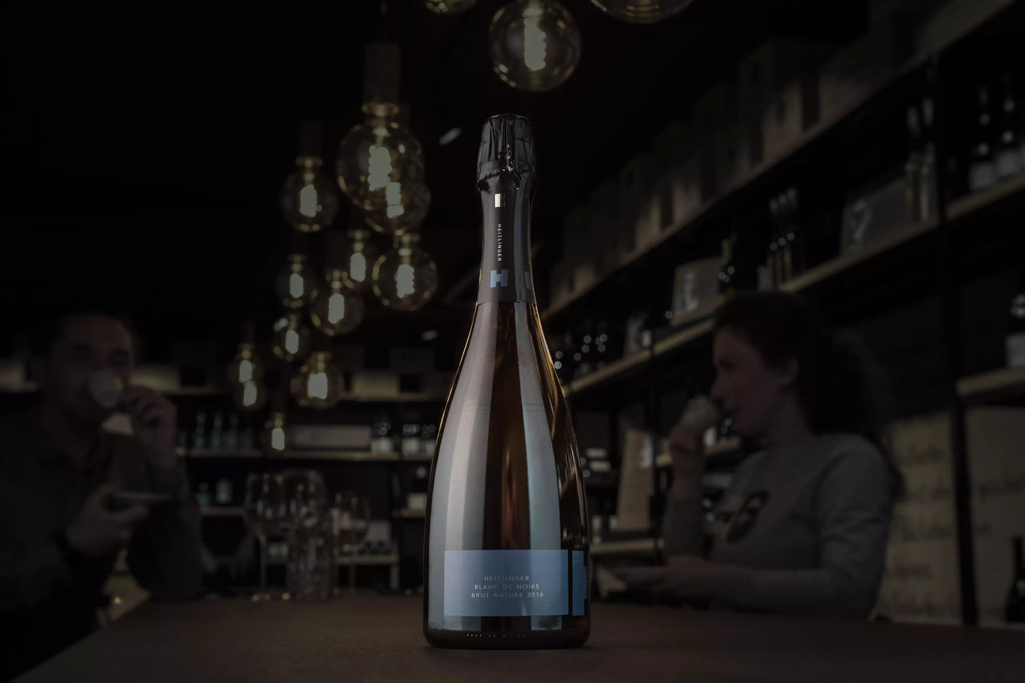 Blanc de Noirs Brut Nature vom Weingut Heitlinger auf dem Tisch in der dunklen Vinothek Hauser.