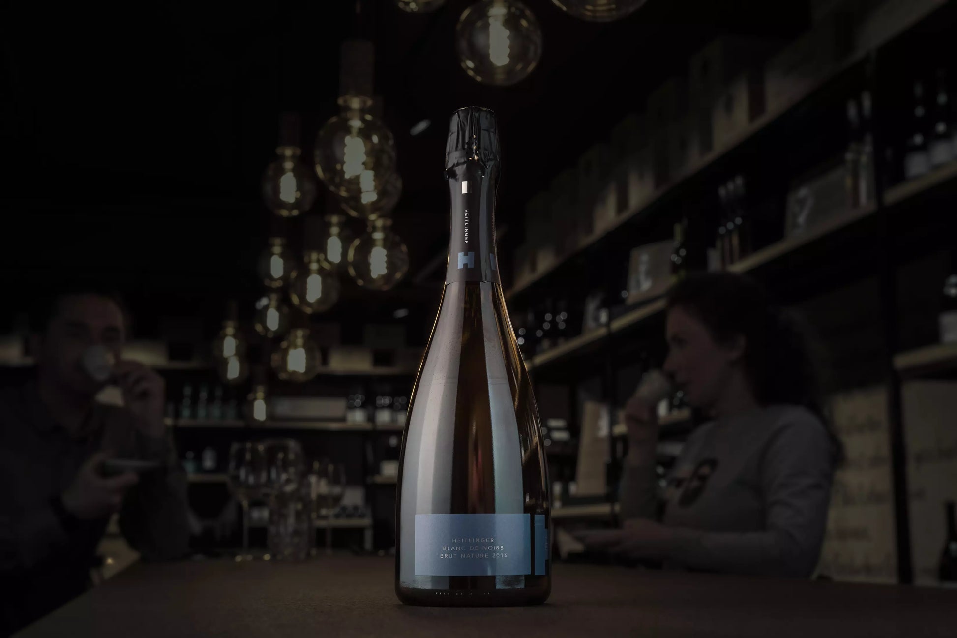 Blanc de Noirs Brut Nature vom Weingut Heitlinger auf dem Tisch in der dunklen Vinothek Hauser.