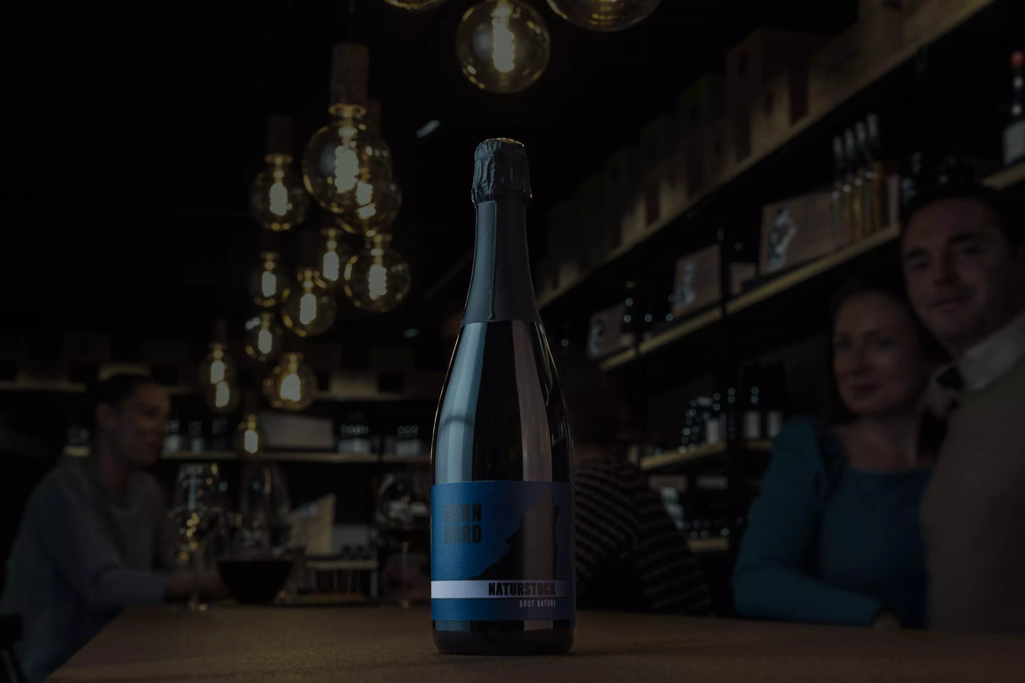 Flasche Naturstück Brut Nature vom Weingut Bernhard auf dem Tisch in der dunklen Vinothek Hauser.
